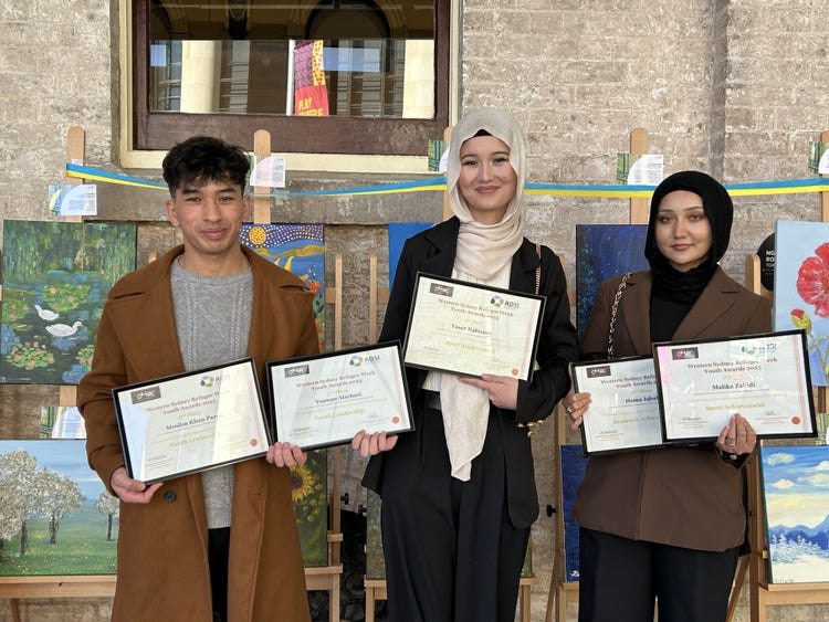 Three students hold up framed Refugee Youth Awards