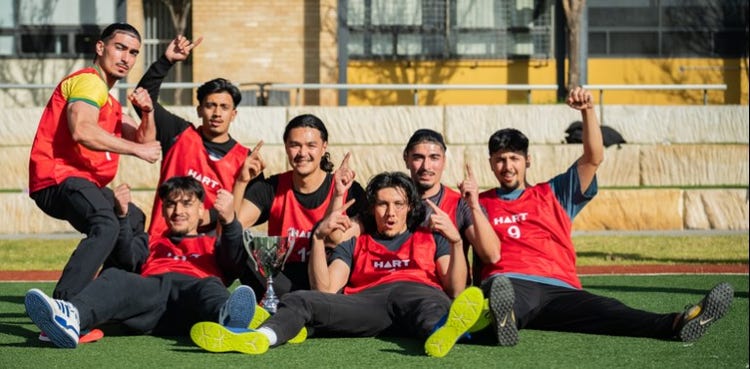 A student soccer team dressed in sportswear wear red bibs and sit together looking happy