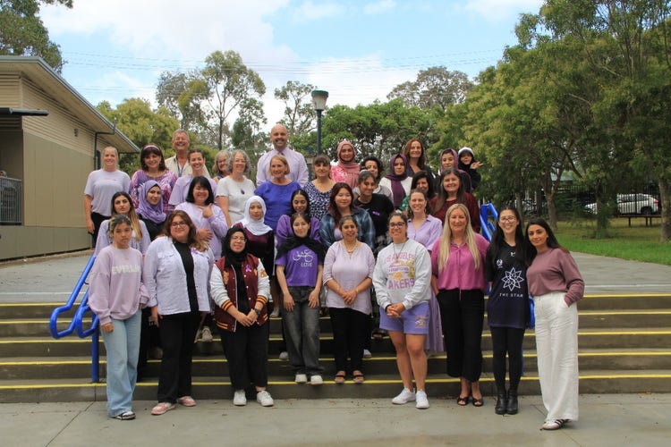 A group of staff and students stand on the steps wearing different items of purple clothing