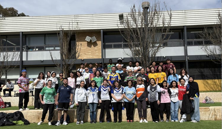 A group of people stand wearing a variety of different sports jerseys in front of a school building