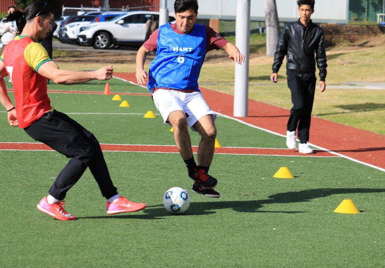 Two students playing soccer on synthetic field